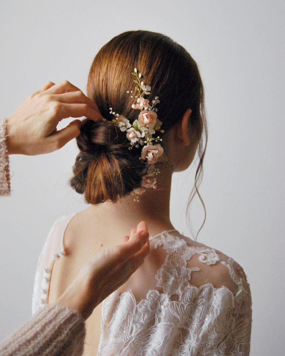 Acconciatura raccolta da sposa con fermaglio floreale di rose rosa e foglie verdi