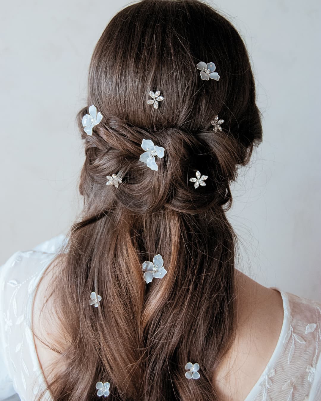 Acconciatura sposa raffinata con fiori bianchi semitrasparenti e punti luce distribuiti nel semi raccolto.