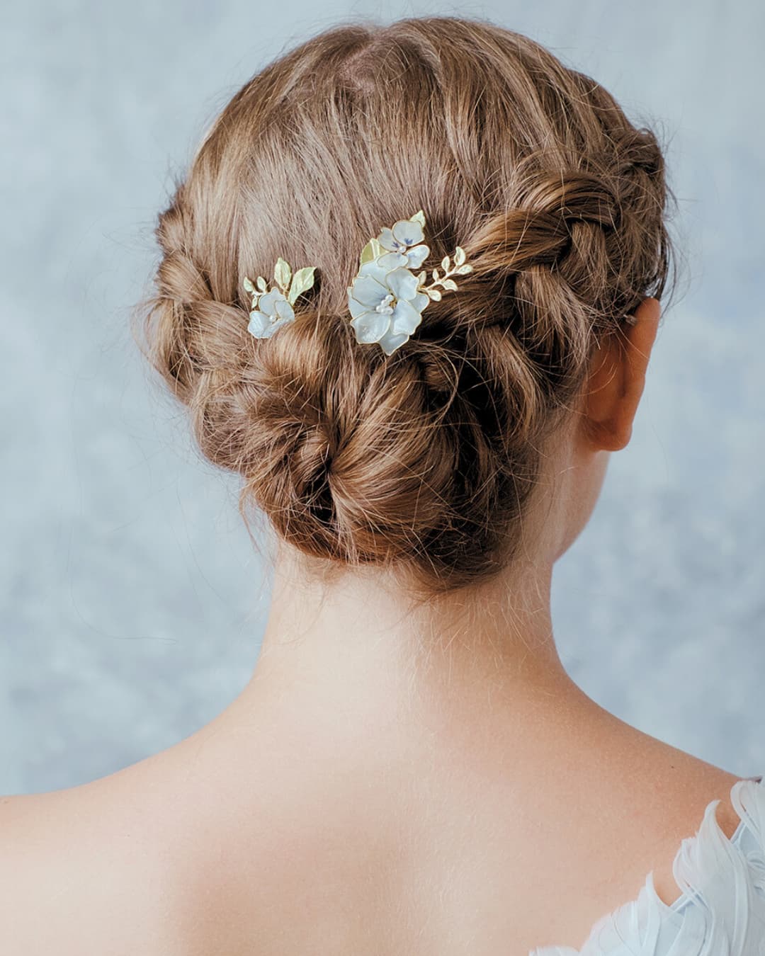 Acconciatura sposa semplice con forcine floreali azzurre artigianali inserite in uno chignon moderno.