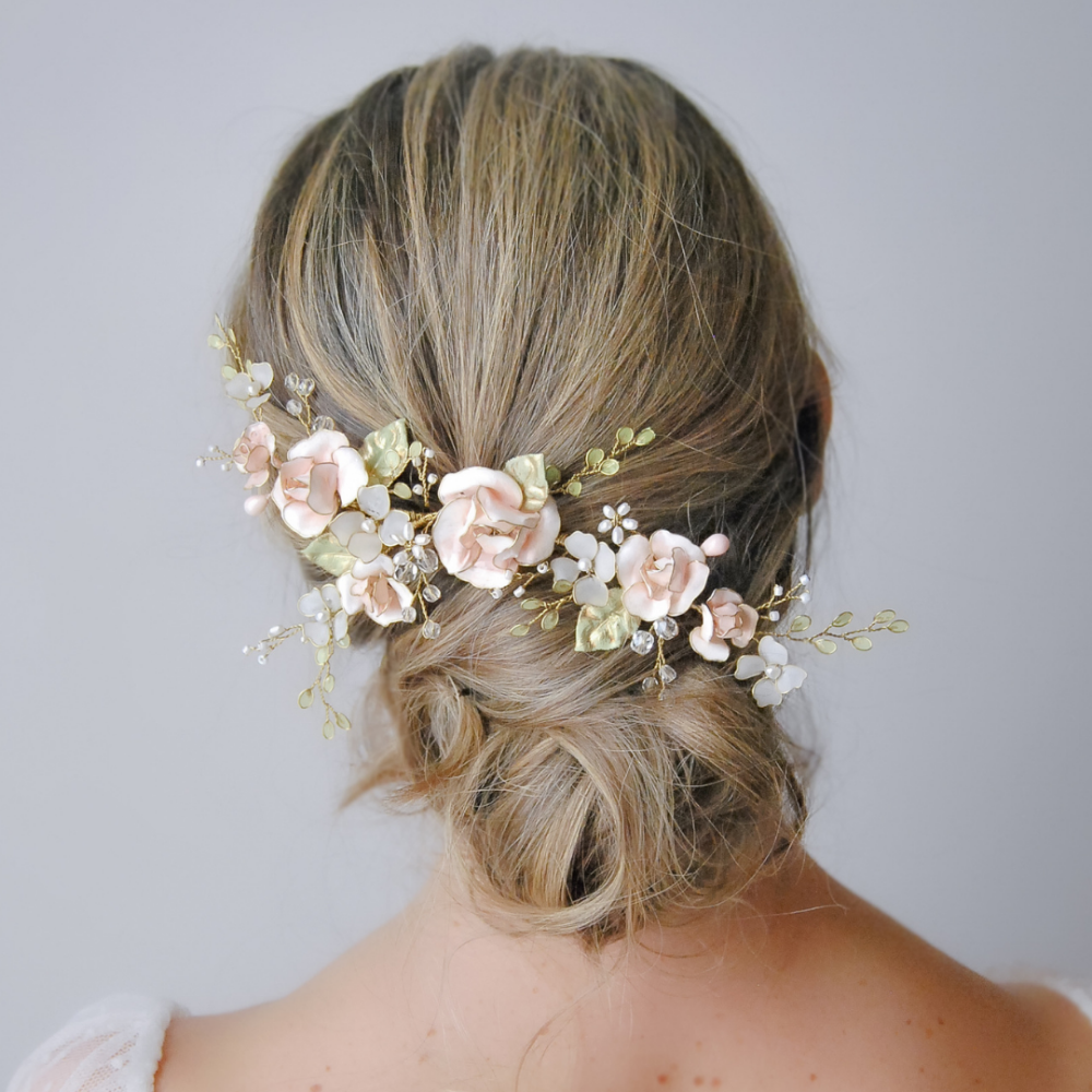Chignon da sposa con fermaglio floreale di rose rosa e foglie verdi, elegante e romantico.