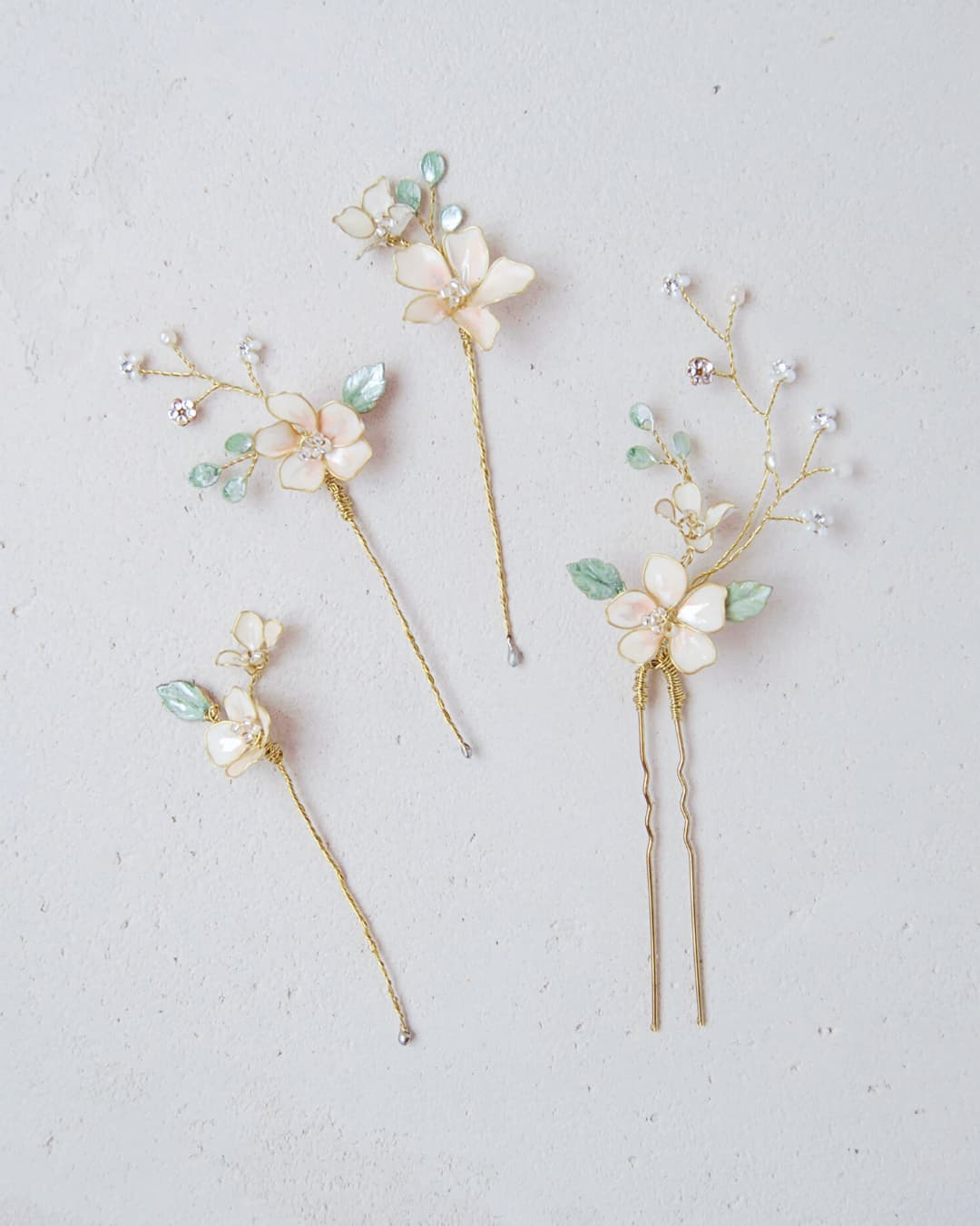 Set di 4 forcine sposa Eden con foglie verdi traslucide, fiori bianchi e rami dorati modellabili a mano.