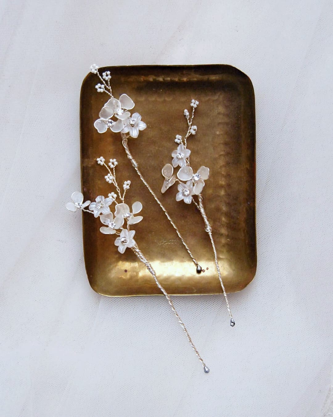 Forcine artigianali Frostalia per sposa con fiori satinati bianchi e cristalli Swarovski su sfondo neutro