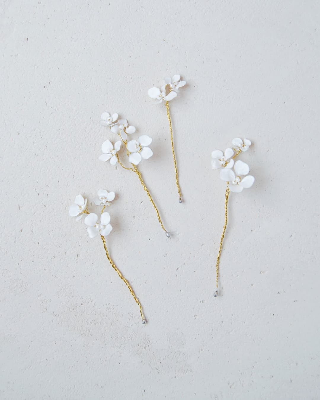 Set di 4 forcine sposa minimal con piccoli fiori bianchi dalla finitura vellutata e rami dorati.