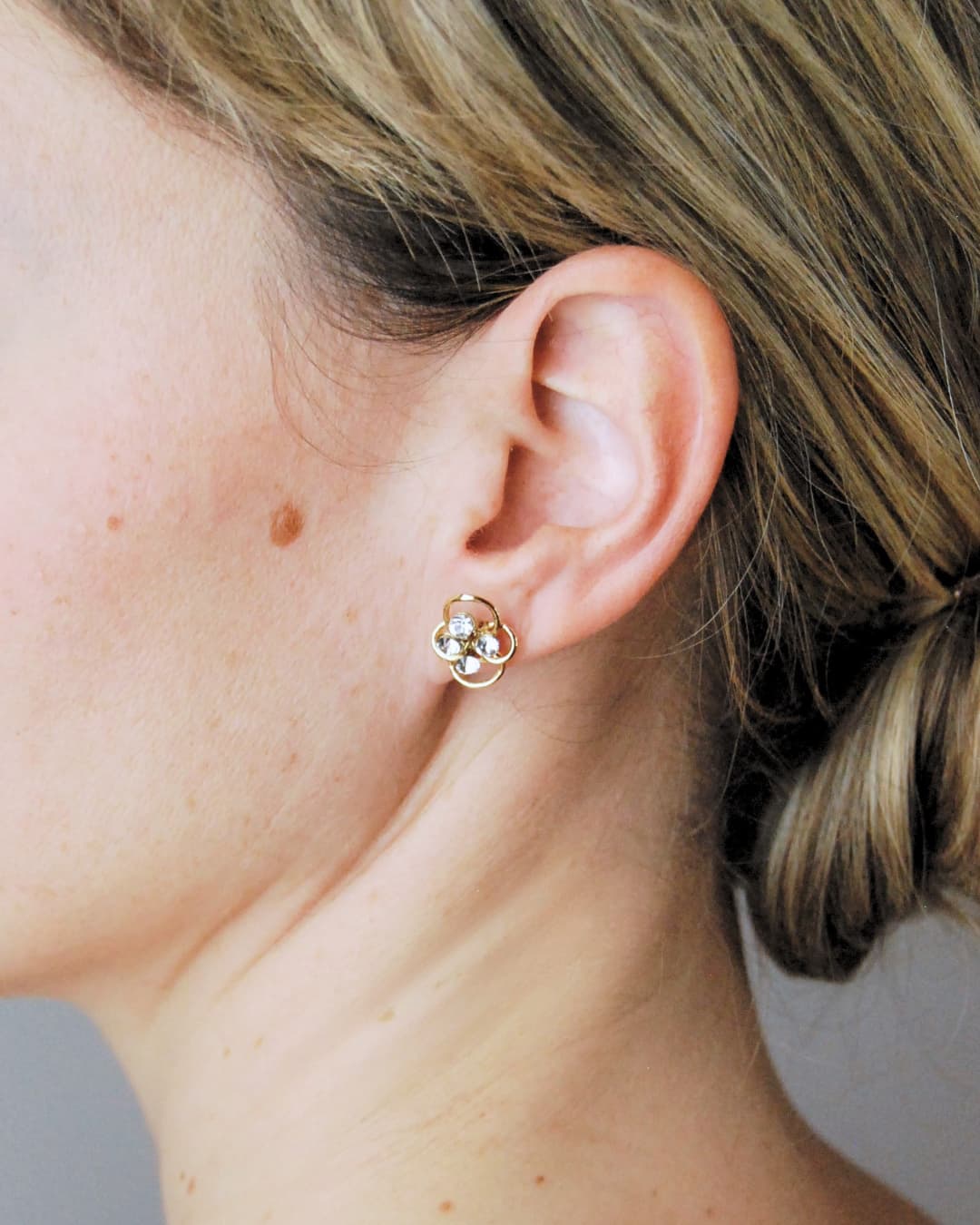 Dettaglio di orecchini dorati con intreccio botanico e quattro strass brillanti per un look sposa di alta gamma.