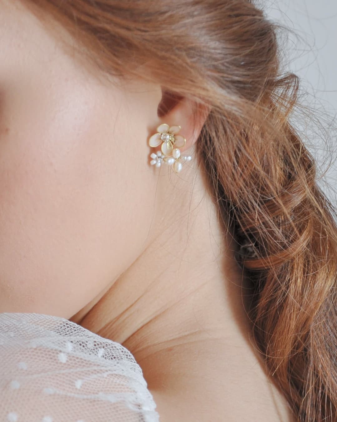 Dettaglio indossato degli orecchini Trinitas in finitura oro con tre fiori differenti e perle di fiume.