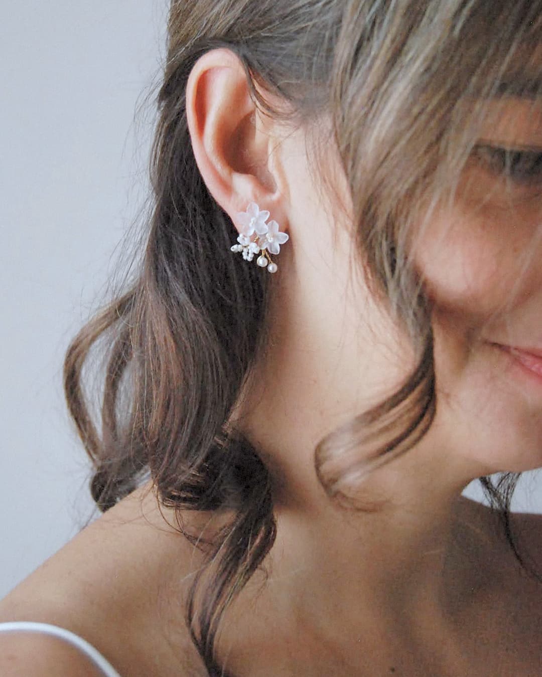 Dettaglio indossato di orecchini a lobo con design botanico frangipane per un bridal look etereo.