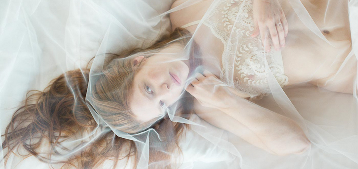 Sposa in lingerie avvolta da un velo da cattedrale distesa su un letto, bridal boudoir elegante e romantico