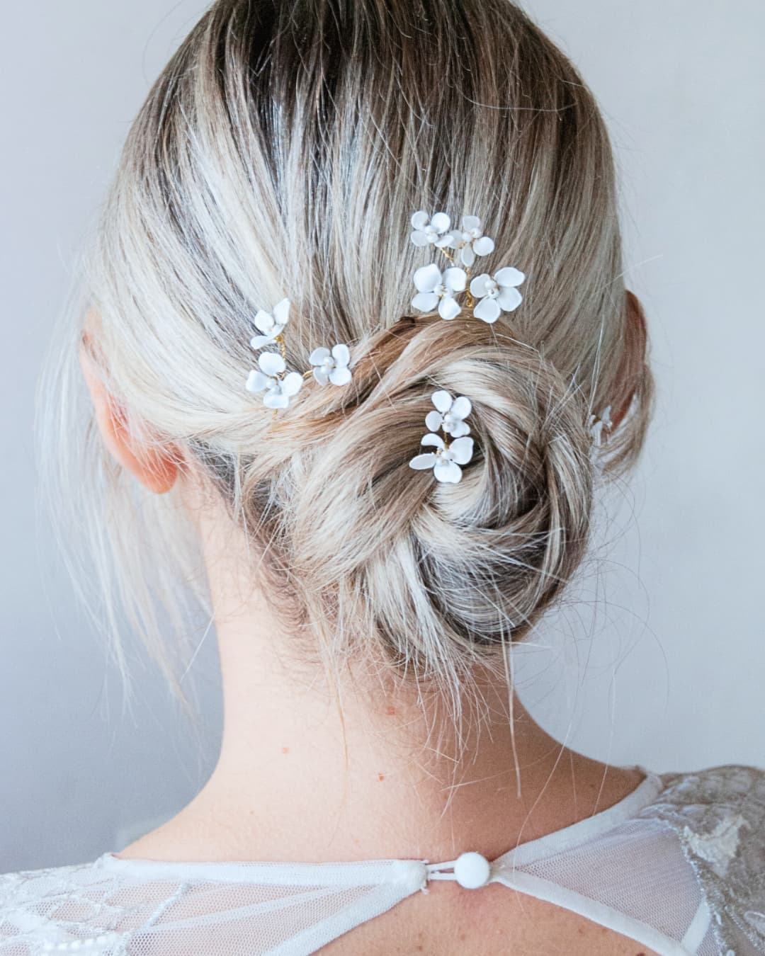 Acconciatura sposa semplice con forcine floreali modellabili inserite in un raccolto morbido e moderno.