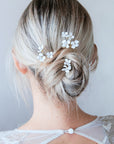 Acconciatura sposa semplice con forcine floreali modellabili inserite in un raccolto morbido e moderno.