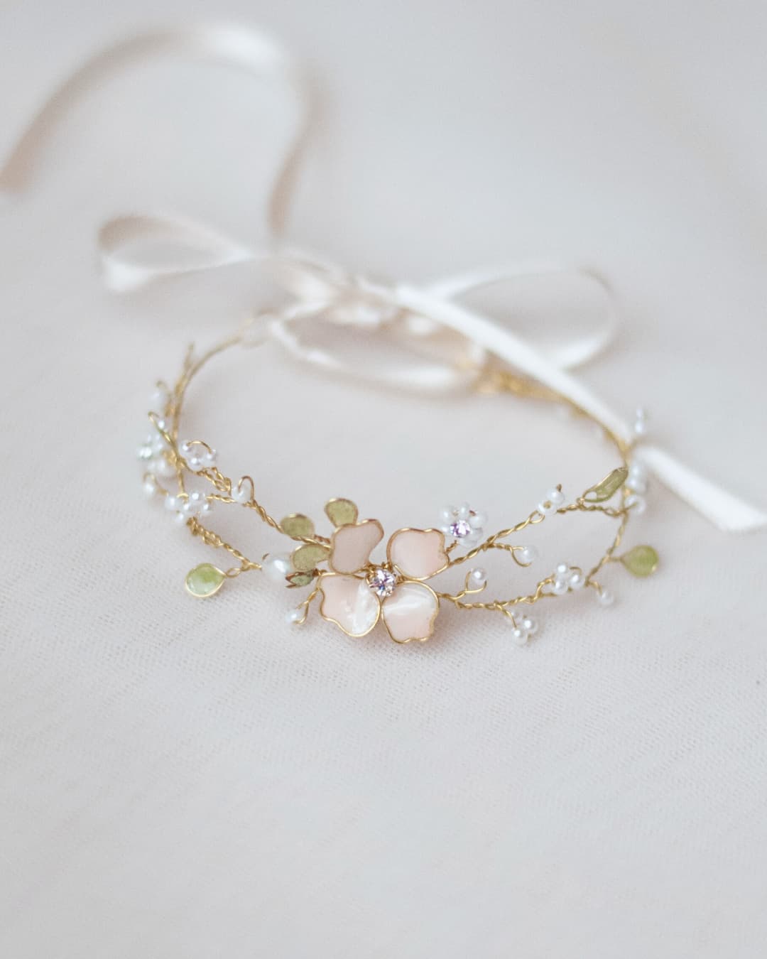 Bracciale sposa Anthis con fiore in smalto rosa cipria, foglie verdi e intreccio di cristalli luminosi.