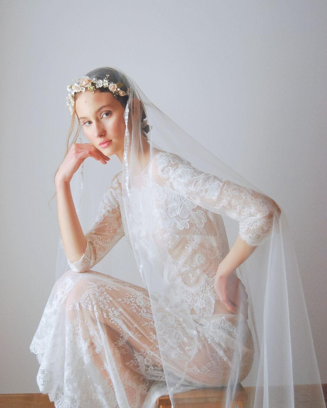 Sposa seduta con coroncina Rosae con rose cipria e velo lungo, abito in pizzo, figura intera - Elibre