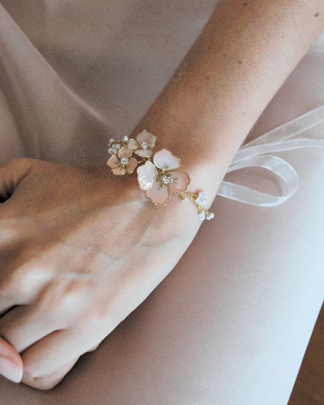 Dettaglio del bracciale Sakura indossato al polso, con petali sfumati e finiture dorate per un look nuziale poetico.