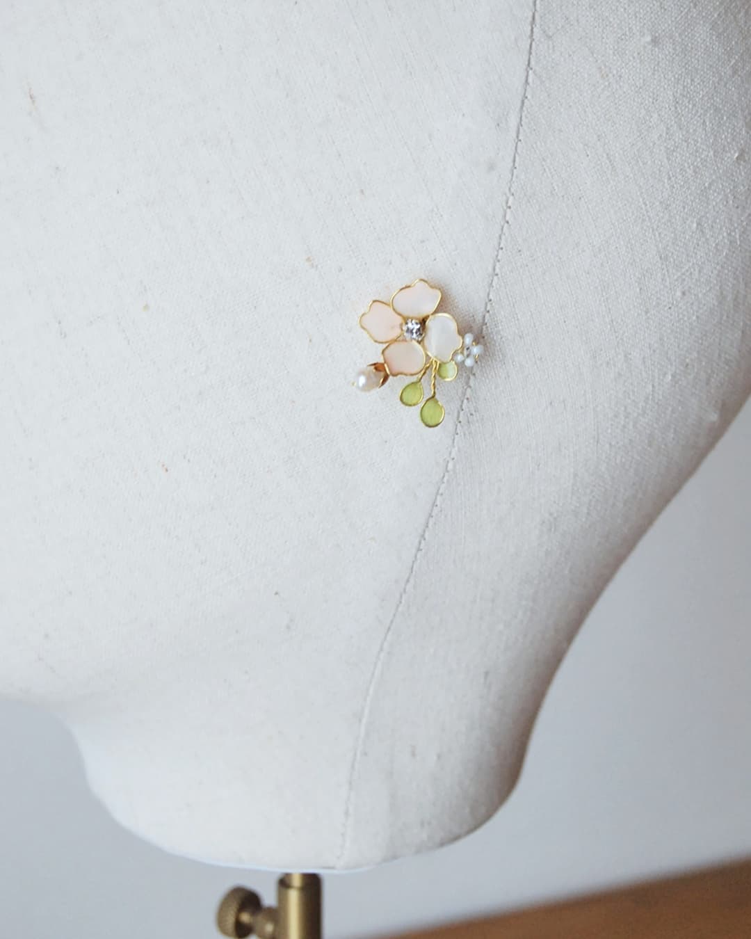 Dettaglio di orecchini floreali fatti a mano con petali color cipria e perle per acconciatura nuziale.