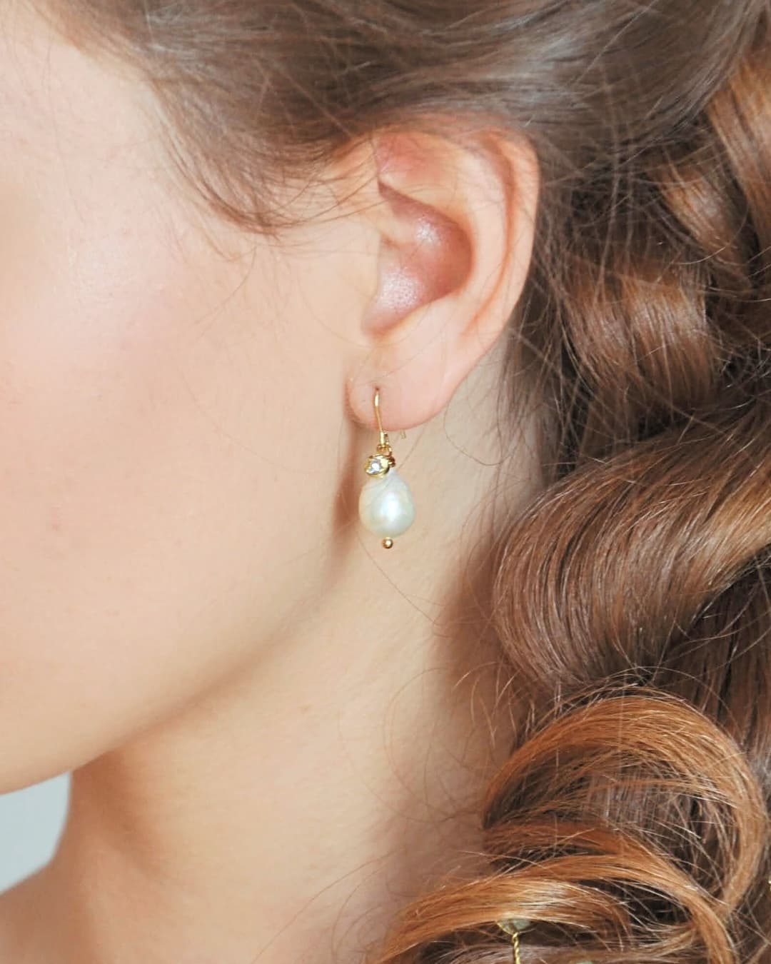 Dettaglio di orecchini a monachella dorata con perle barocche naturali e charm in cristallo brillante.